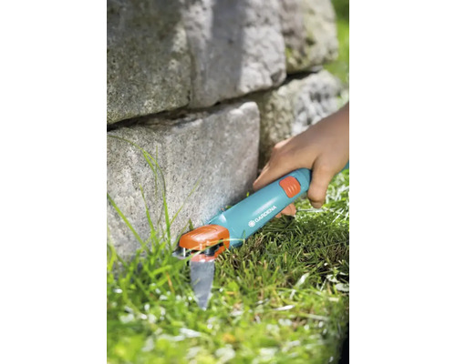 Gardena Grasschere im Einsatz zum Trimmen von Rasenkanten neben einer Steinmauer.