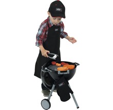 Kind spielt mit einem Weber Kindergrillset, bestehend aus Grill, Grillzange, Spielzeug Lebensmitteln, Schürze, Mütze und Grillhandschuh