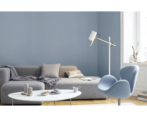 Wohnzimmer mit grauer Couch, weißem Tisch und blauem Sessel vor blauer Wand