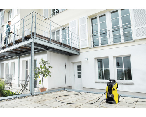 Frau reinigt Terrasse mit Hochdruckreiniger vor Hausfassade