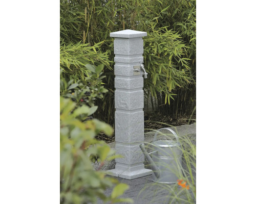 Gartenzapfstelle aus Stein mit Wasserhahn und Gießkanne im Garten