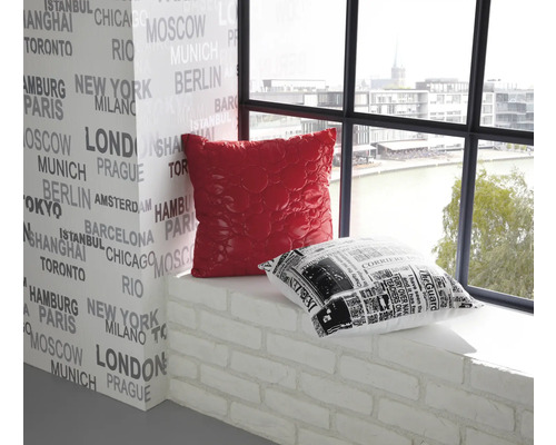 Dekoratives Interieur mit einem roten und einem schwarz-weißen Kissen auf einer Fensterbank vor einer mit Stadtnamen bedruckten Wand