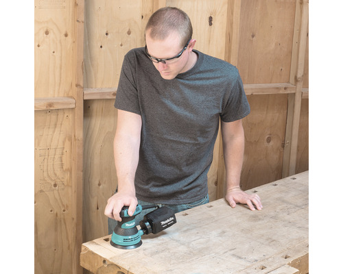 Mann schleift Holzbrett mit einem Makita Exzenterschleifer