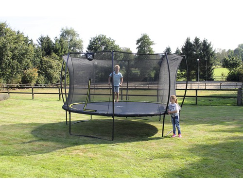 Trampolin mit Sicherheitsnetz im Garten, auf dem ein Kind springt, während ein anderes daneben steht.