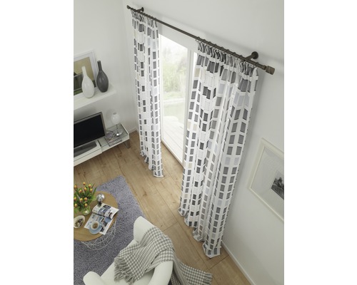 Wohnzimmer mit Fensterdekoration, bestehend aus Vorhängen mit grafischem Muster und Vorhangstange.