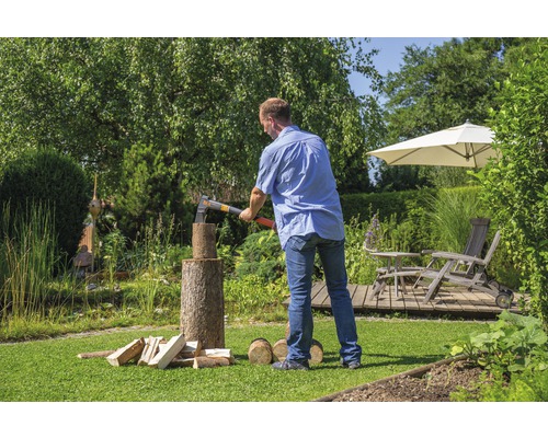 Mann spaltet Holz mit einer Axt im Garten.