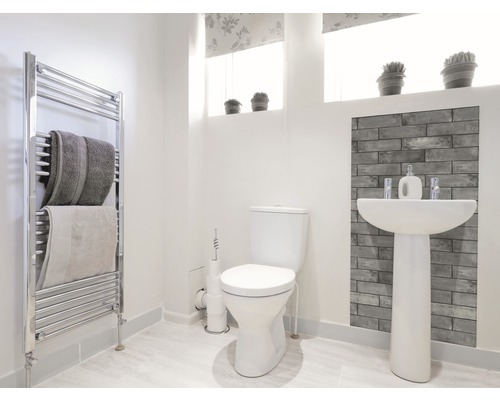 Helles Badezimmer mit Toilette, Waschtisch, Heizkörper und Handtüchern.