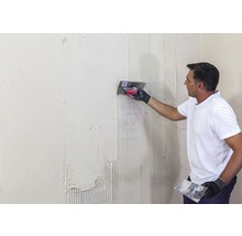 Ein Mann trägt Fliesenkleber mit einer Glättkelle auf eine Wand auf.