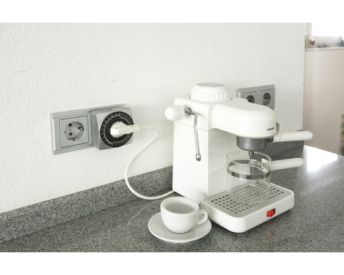 Zeitschaltuhr in Steckdose neben Kaffeemaschine mit Tasse