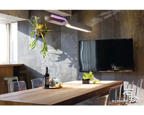 Esszimmer mit Holztisch, Stühlen, Lampe und Fernseher an einer Steinwand.