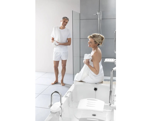 Badezimmer mit Badewanne und Badewannenlift sowie zwei Personen mit Handtüchern