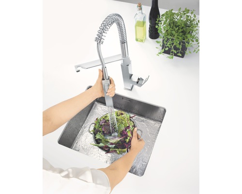 Eine Küchenspüle mit einer Person, die Gemüse unter einem Wasserhahn mit Spiralfeder wäscht.