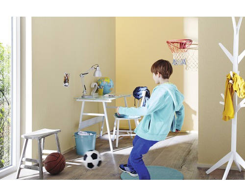 Kind spielt im hellen Kinderzimmer mit Schreibtisch, Stuhl, Lampe, Basketballkorb und Fußball