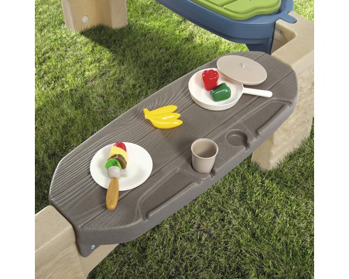 Detailansicht eines Spieltisches mit Spielzeuglebensmitteln im Garten.