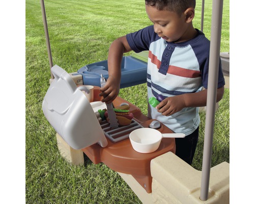 Kind spielt mit einem Spielzeuggrill im Freien