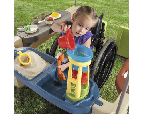 Mädchen im Rollstuhl spielt mit einem Spieltisch für Wasser und Sand im Freien