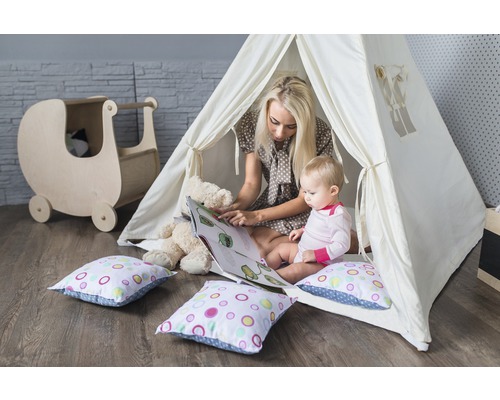 Mutter liest Kind in einem Spielzelt ein Buch vor, mit Spielzeugwagen und Kissen im Kinderzimmer.