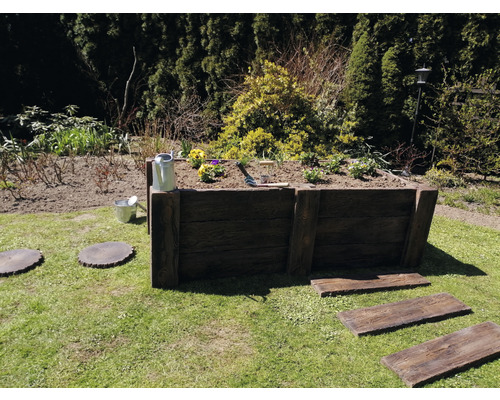 Hochbeet aus Holz im Garten mit Bepflanzung, Gießkanne und Gartengeräten