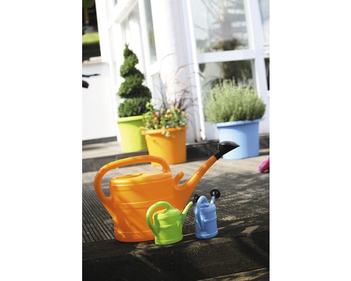 Drei Gießkannen in unterschiedlichen Größen vor bepflanzten Blumentöpfen