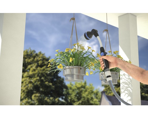 Eine Person bewässert hängende Blumenkästen mit einer Gartenspritze.