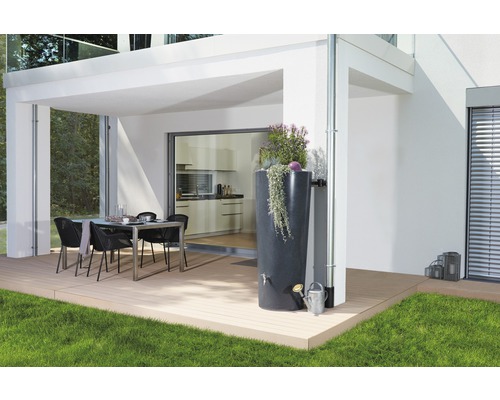 Szene im Außenbereich mit einer Regentonne neben einem Fallrohr, einer Gießkanne und einem Esstisch auf einer Terrasse