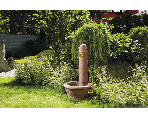Gartenbrunnen aus Stein mit Wasserhahn in grüner Gartenumgebung.