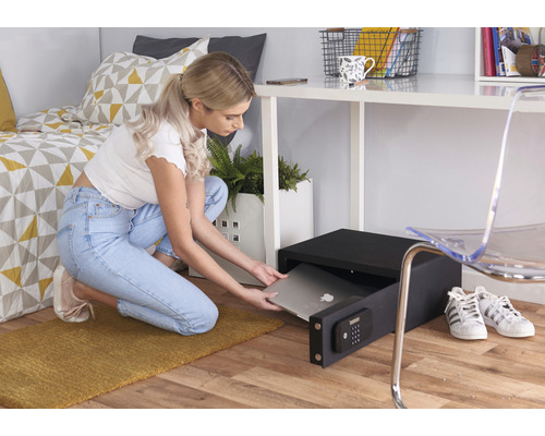 Eine Frau verstaut einen Laptop in einem schwarzen Möbeltresor in einem Zimmer