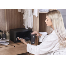 Frau legt eine Uhr in einen Möbeltresor in einem Schrank.