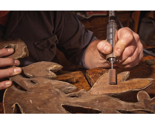 Handwerker bearbeitet Holzschnitzerei mit Rotationswerkzeug.