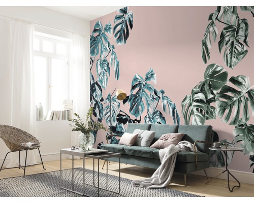 Wohnzimmer mit Monstera-Motivtapete, Sofa und Rattansessel.