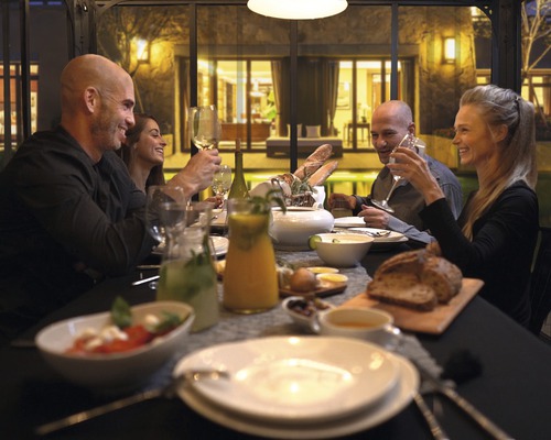 Gruppe von Personen sitzt an einem Tisch mit Speisen und Getränken in einem Wintergarten.