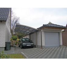 Carport und Garage aus Stein mit gepflasterter Zufahrt und parkendem Auto