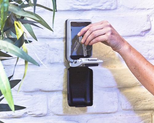 Schlüsselsafe zur Schlüsselaufbewahrung an einer Wand mit Schlüsselentnahme durch eine Person