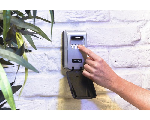 Master Lock Schlüsselsafe mit Zahlencode an einer Wand montiert, eine Hand bedient das Schloss