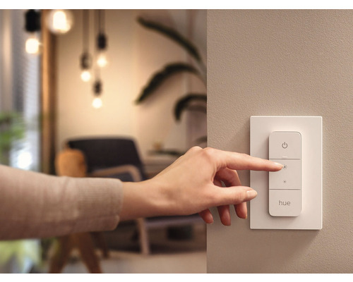Eine Hand bedient einen Philips Hue Dimmschalter an der Wand.