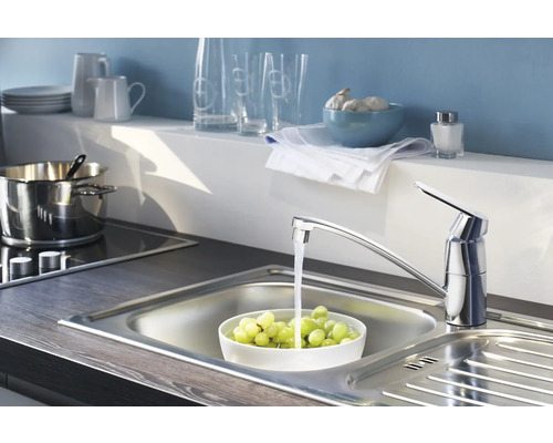 Spültischarmatur mit fließendem Wasser in einer Edelstahlspüle, gefüllt mit Weintrauben in einer Küche