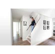 Helles Treppenhaus mit Frau auf der Treppe und aufgehängten Bilderrahmen