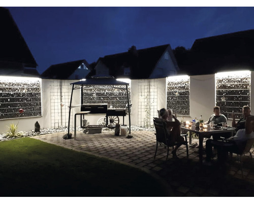 Abendliche Gartenszene mit Grill, Gabionenwänden und sitzenden Personen