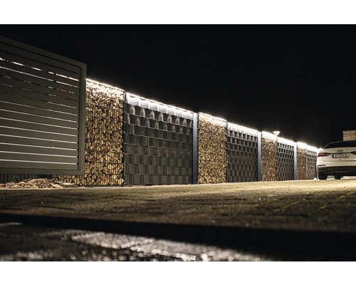 Gabionenwand mit Holzbefüllung und angrenzendem Zaun bei Nacht