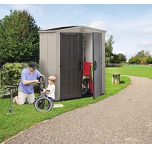 Gartenszene mit Gerätehaus, in dem Gartengeräte und ein Kinderfahrrad aufbewahrt werden, während ein Vater mit seinem Sohn ein Fahrrad repariert