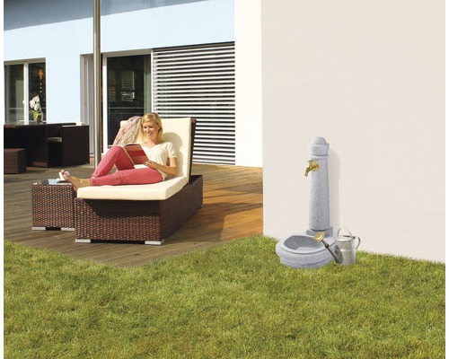 Szene im Garten mit Liegestuhl, Brunnen und lesender Frau