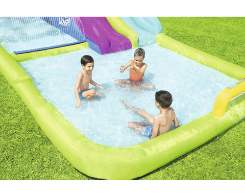 Aufblasbarer Pool mit Wasserrutsche und spielenden Kindern im Garten.