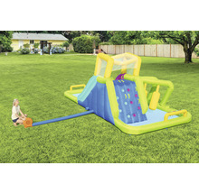 Aufblasbarer Wasserpark mit Rutsche, Kletterwand und Pool im Garten, eine Frau pumpt Luft hinein.