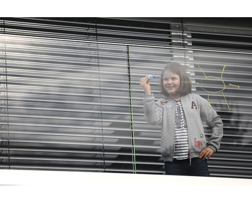 Mädchen malt mit Kreide auf ein Fenster mit Jalousien