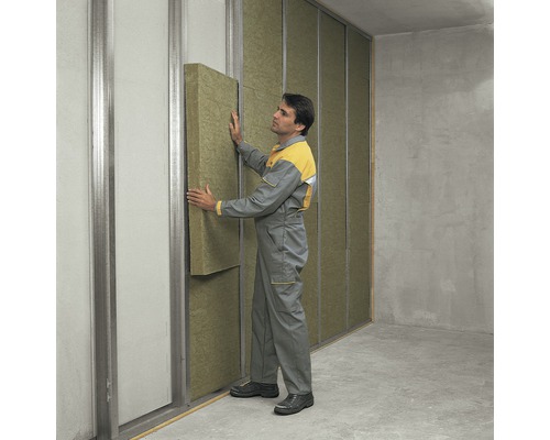 Ein Mann montiert eine Dämmplatte an einer Wand mit Metallrahmen für die Innenisolierung.