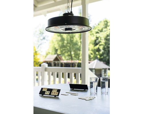 Szene mit einem Hängeheizstrahler über einem Tisch mit Gläsern und einem Spiel im Freien