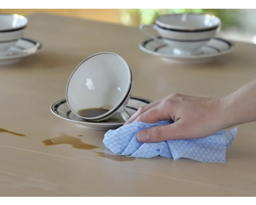 Eine Hand wischt mit einem Tuch eine verschüttete Flüssigkeit von einem Tisch.