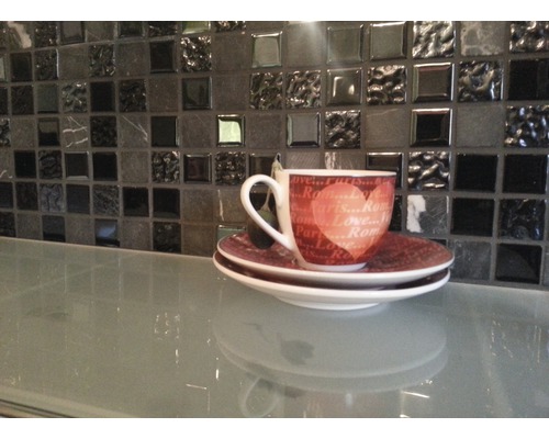 Tasse mit Untertasse auf einem Tisch vor einer Mosaikwand