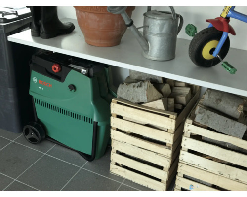 Szene mit einem Häcksler, Gummistiefeln, einem Übertopf, einer Gießkanne, einem Dreirad und Holzkisten.