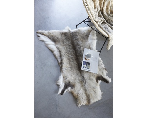 Dekoratives Rentierfell auf dem Boden neben einem Stuhl und einer Zeitschrift.